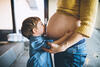 Ein Kind küsst seiner Mutter auf ihren Schwangerschaftsbauch