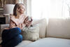 Frau sitzt mit einem Tee auf der Couch und schaut nach draußen.