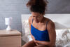 Frau sitzt auf dem Bett und krümmt sich vor Bauchschmerzen