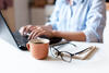 Frau am PC mit Notizen, Brille und Kaffeetasse auf dem Tisch