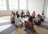 Gruppe von Frauen und Männern sitzt in einem Fitnesskurs auf im Kreis angeordneten Matten