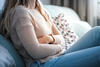 Junge Frau mit Bauchschmerzen sitzt auf dem Sofa  