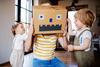 Vater mit Karton auf dem Kopf spielt Roboter mit seinen Kindern
