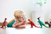 Junge spielt mit Dinofiguren allein auf dem Fußboden