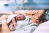 Mutter im Kreißsaal weint nach der Geburt mit Baby im Arm