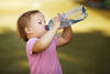 Kleinkind im Schatten trinkt auf einer Wiese aus einer Wasserflasche
