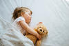 Kind schläft mit Teddy im Bett