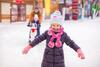 Kleines Mädchen im Schnee mit Vater und Schwester im Hintergrund