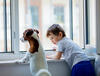 Kleinkind steht neben einem Hund am offenen Fenster