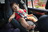 Kleinkind schläft in Sommerkleidung auf dem Autorücksitz im Kindersitz und wirkt erschöpft