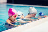 Kinder im Schwimmunterricht halten sich zwischen ihrer Schwimmlehrerin am Beckenrand fest