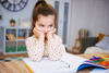 Grundschülerin macht Hausaufgaben wirkt unkonzentriert und guckt in die Luft anstatt aufs Übungsheft