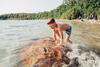 Grundschulkind mit Taucherbrille klettert im See auf einen Stein