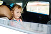 Kleinkind sitzt bei offenem Fenster im Autokindersitz und schaut heraus