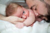 Vater hält Augen geschlossen und streicht mit Nasenrücken über den Arm seines Babys