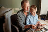 Junge sitzt auf dem Schoß seines Großvaters und schaut sich Fotos an
