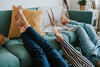 Mutter und zwei Kinder liegen auf dem Fußboden und legen die Beine hoch auf die Couch