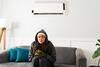Frau sitzt frierend vor einer Klimaanlage