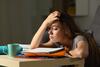 Junge Frau am Schreibtisch greift sich gestresst vom Lernen an den Kopf