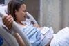 Frau liegt mit Geburtswehen im Klinikbett und hält sich mit einer Hand am Bett fest