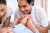 Eltern kommunizieren und lachen mit ihrem Baby, das vor ihnen liegt und die Hände nach dem Vater ausstreckt