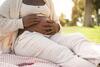 Afrikanische schwangere Frau sitzt in einem Park auf einer Decke und hält ihren Bauch