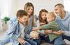 Mann und Frau spielen im Sitzen mit drei Kindern und stecken Münzen in ein Sparschwein