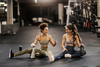Zwei sportliche Frauen sitzen nach dem Training auf dem Boden eines Gym