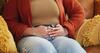 Person sitzt mit Unterleibsschmerzen auf dem Sofa und hält die Hände an den Bauch